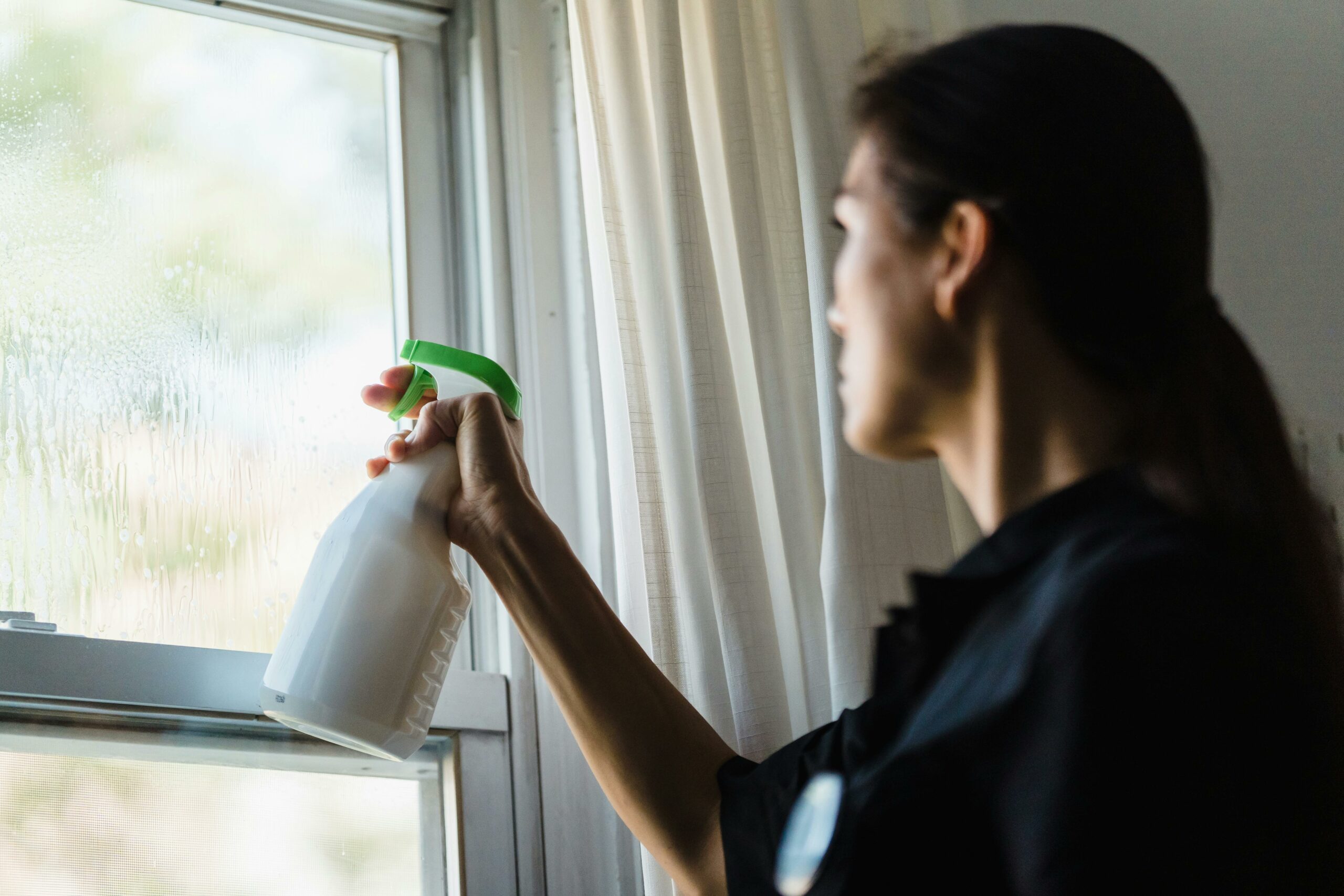 Brown-haired woman using a vinegar spray to clean a window.