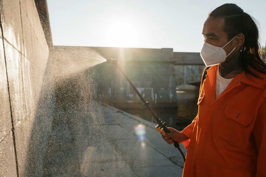 Man in Orange Robe Cleaning Gray Concrete Wall.