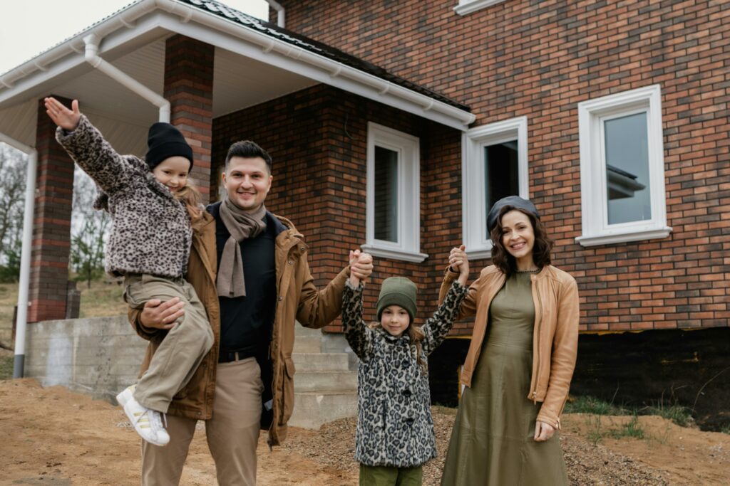 Happy family standing in front of a brick house, raising hands together—capturing the pride of homeownership and raising the question: can you power wash a brick house?