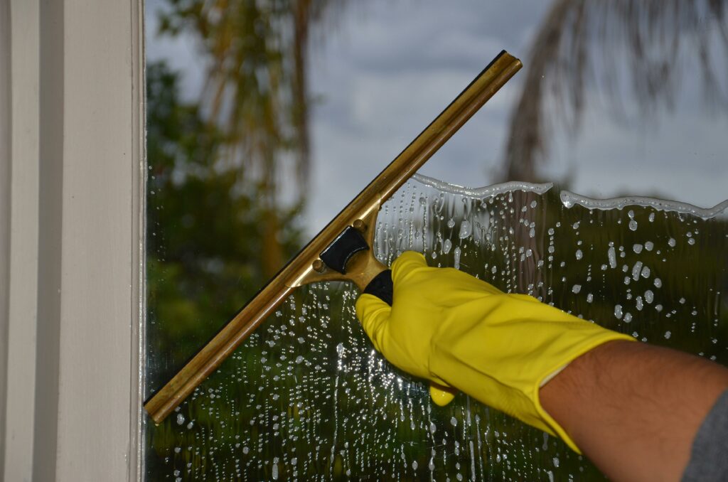 Close-up of a person wearing a yellow glove using a squeegee to clean a window, highlighting the importance of professional window cleaning for curb appeal.