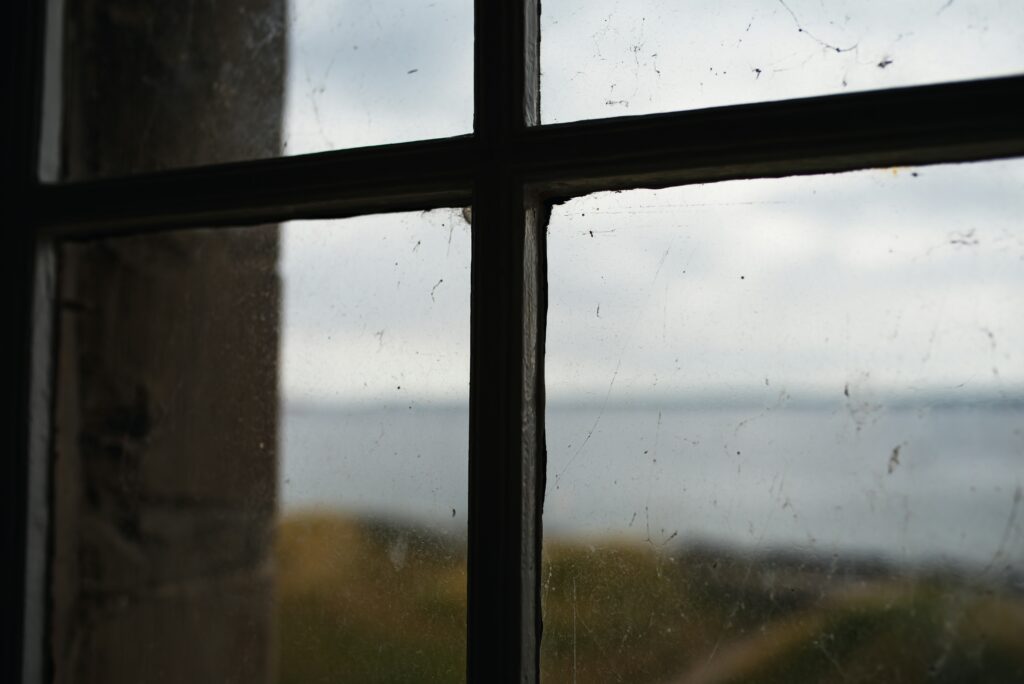Close-up of a dirty window with smudges and streaks, overlooking a cloudy seascape in the background.