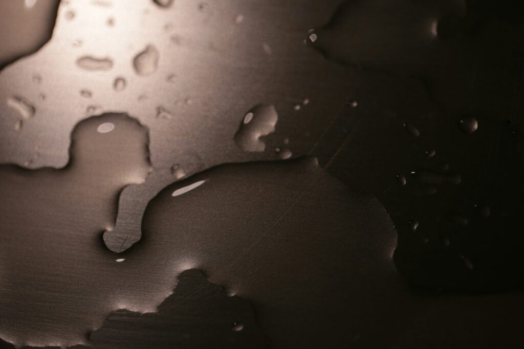 Close-up of water droplets scattered on a dark smooth surface with soft reflections. 