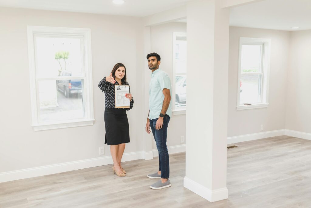 Real estate agent showing a property to a potential buyer inside a bright modern home, holding documents while discussing details.